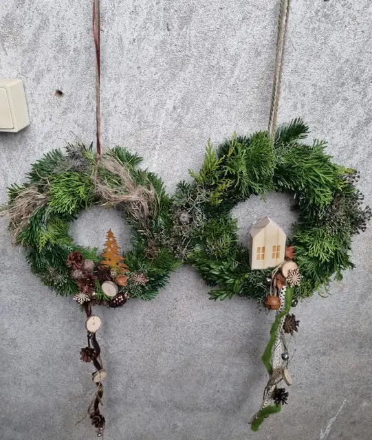 Zwei natürliche Türkränze mit Holzbäumchen und Holzhaus an einer Betonwand